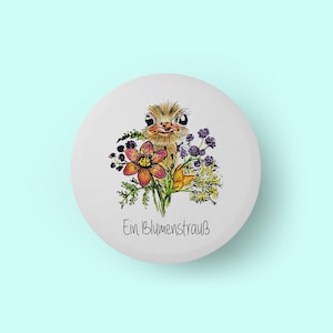 Könnte beinhalten: Ein weißer, runder Knopf mit einer Aquarellillustration eines Straußes, der einen Blumenstrauß hält. Die Blumen sind in Rot-, Lila- und Gelbtönen gehalten. Der Text "Ein Blumenstrauß" steht in schwarzer Schrift darunter.