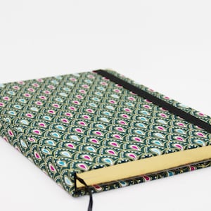 May include: A green journal with a gold-colored spine and a black elastic band closure. The cover features a repeating pattern of teal, pink, and gold teardrop shapes.