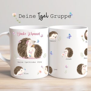 Op de afbeelding: Witte keramische mok met een aquarel illustratie van egels, vlinders en bloemen. De mok heeft de tekst "Danke Johanna!" en "Deine Igelkinder 2024". Extra namen staan op de mok.