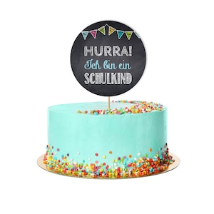 May include: A turquoise cake with colorful sprinkles and a black chalkboard cake topper that says "HURRA! Ich bin ein SCHULKIND"