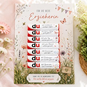 Könnte beinhalten: Eine rechteckige Karte mit einer Blumenwiesen-Illustration, dem deutschen Text "FÜR DIE BESTE Erzieherin" und sieben Schokoriegeln mit der Aufschrift "du" und deutschen Dankessprüchen, die vertikal in der Mitte der Karte angeordnet sind.