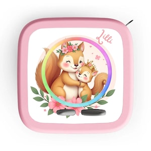 May include: Pink square container featuring a cartoon illustration of two squirrels embracing. The squirrels are brown, wearing floral crowns, and surrounded by a rainbow circle and pink flowers. The name "Lilli" is written in cursive.