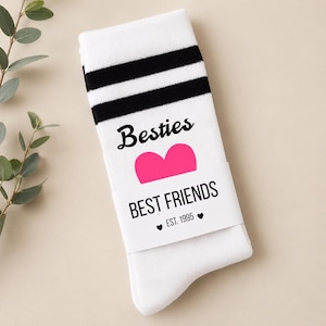 Puede incluir: Calcetines blancos con rayas negras en la parte superior. Los calcetines tienen la palabra "Besties" encima de un coraz&oacute;n rosa, y "BEST FRIENDS" con "EST. 1995" debajo. Un gran regalo para una mejor amiga.