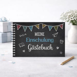 Peut inclure: Un livre d'or &agrave; spirales avec une couverture de style tableau noir. La couverture pr&eacute;sente le texte allemand "Meine Einschulung G&auml;stebuch" en blanc et bleu, avec des dessins d&eacute;coratifs et une banni&egrave;re color&eacute;e. Un crayon repose sur la surface.
