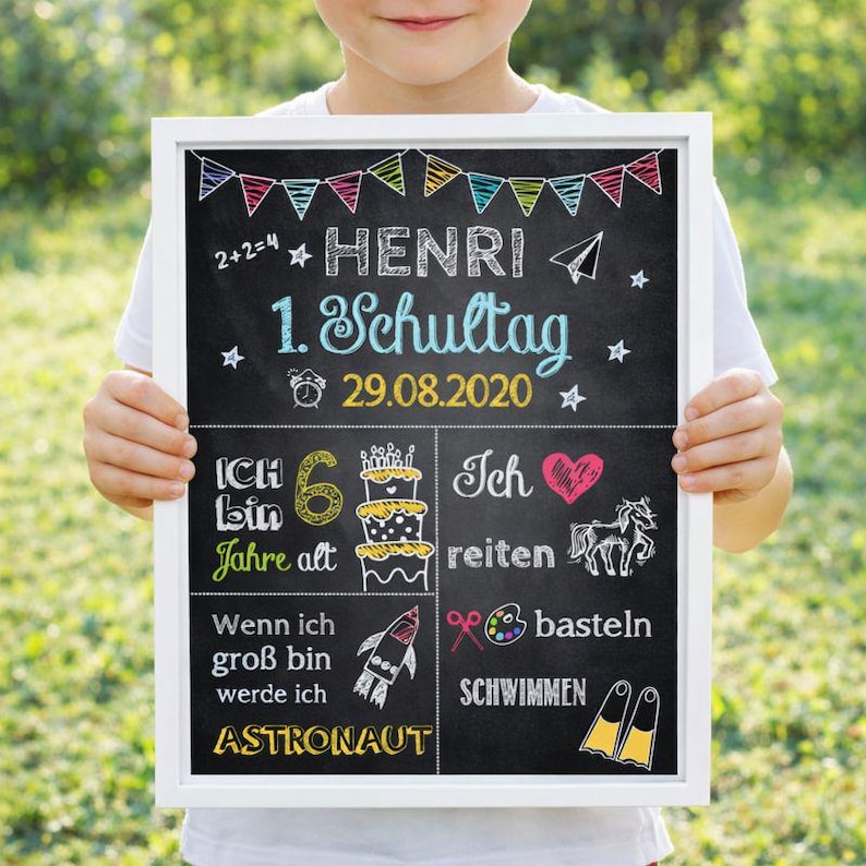 Peut inclure: Une ardoise encadr&eacute;e, tenue par une personne. Le tableau noir affiche du texte et des illustrations blancs et color&eacute;s. Il comprend le nom "HENRI", la date "29.08.2020", et des phrases comme "1. Schultag" et "Astronaut".