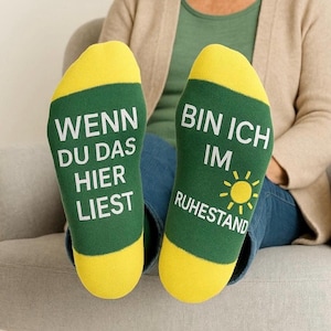 Könnte beinhalten: Ein Paar grün-gelbe Socken mit weißem Text. Eine Socke trägt den Schriftzug "Wenn du das hier liest, bin ich im Ruhestand". Die andere Socke trägt den Schriftzug "Bin ich im Ruhestand".