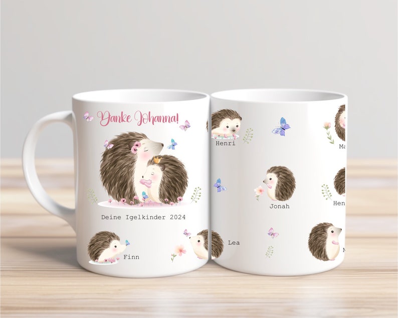 Op de afbeelding: Witte keramische mok met een aquarel illustratie van twee egels met de tekst "Danke Johanna!" en "Deine Igelkinder 2024". De mok heeft ook kleinere egel illustraties met namen en vlinders.