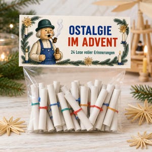 Può includere: Un sacchetto di plastica trasparente contenente numerosi piccoli rotoli di carta bianca fissati con elastici colorati. L'intestazione illustrata mostra un uomo con una pipa e il testo OSTALGIE IM ADVENT 24 Lose voller Erinnerungen.
