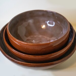 May include: Three brown ceramic bowls nested together. The bowls are glazed and have a rustic appearance.
