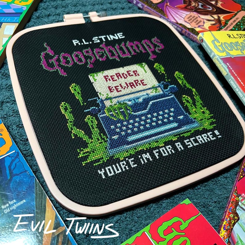 May include: A black cross-stitch featuring the text "Goosebumps" and "Reader Beware" with a typewriter design. The design includes green slime and the phrase "You're in for a scare!" surrounded by Goosebumps books.