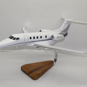 Può includere: Un modello di aereo bianco e grigio con ali argentate e una base in legno. Il modello ha il numero N18776 sul lato. L'aereo è una replica in miniatura di un jet.