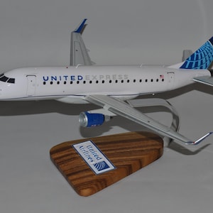 Può includere: Un modellino di aereo bianco con dettagli blu. L'aereo ha scritto "UNITED EXPRESS" sul lato e un logo United Airlines sulla coda. L'aereo è su un supporto di legno con un logo United Airlines.