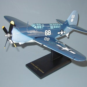 Op de afbeelding: Een blauw en wit modelvliegtuig met het nummer 68 aan de zijkant. Het model staat op een zwarte standaard met de tekst "Curtiss SBC Helldiver Model 1/48" erop.