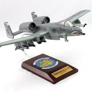 May include: A gray Fairchild A-10 model airplane with a shark mouth design on the nose. The model is mounted on a wooden base with the text "FAIRCHILD A-10" and "SCALE 1/48". The wings are light gray.