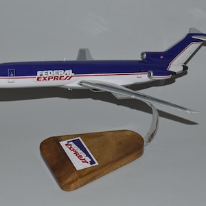 May include: A model airplane with a blue and white fuselage, featuring the "FEDERAL EXPRESS" logo. The model is mounted on a wooden base with a metal support. The plane has silver wings and tail fins.
