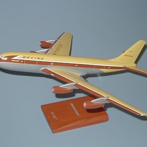 May include: A brown and beige model airplane with the text "BOEING" and "N70100" on the side. The model is on a wooden base.