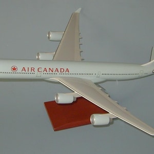 Può includere: Un modello di aereo Airbus A330-300 di Air Canada bianco con accenti rossi e una bandiera canadese sulla coda. Il modello è su un piedistallo di legno.