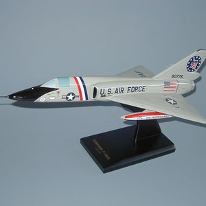 May include: A white and gray model airplane with black accents. The plane has a red, white, and blue star on the side and the words "U.S. AIR FORCE" printed on the fuselage. The tail of the plane has a red, white, and blue circle with the number "76" in the center. The plane is sitting on a black stand with the words "CONVAIR F-106" printed on it.