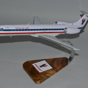 Può includere: Un modellino di aereo bianco, rosso e blu con la scritta "American Eagle" sul lato. L'aereo è su un supporto in legno con il logo American Eagle.