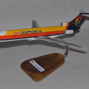 Può includere: Un modello di aereo con una combinazione di colori giallo, arancione e blu, con il logo "air Jamaica" sulla fusoliera e una base di legno. Il modello è una replica dettagliata di un aereo di linea commerciale.