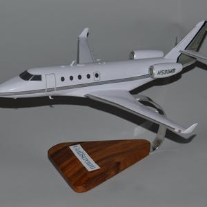 Puede incluir: Un modelo de avión blanco con detalles en negro y plata, montado sobre una base de madera. El modelo tiene el número de registro N591MB y el nombre "Gulfstream" en la base. La aeronave tiene dos motores y un diseño elegante.