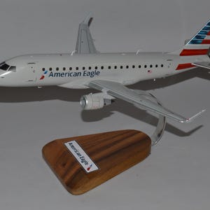 Può includere: Un modello di aereo American Eagle, bianco con il logo della compagnia aerea e il design della coda. Il modello è montato su una base di legno con il nome della compagnia aerea. L'aereo ha ali e motori dettagliati.