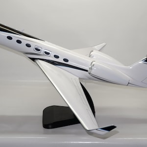 Könnte beinhalten: Ein weißes und schwarzes Modellflugzeug mit elegantem Design. Das Modell hat einen schwarzen Sockel, Flügel und Heck, mit einem weißen Körper und schwarzen Akzenten. Das Flugzeug hat mehrere Fenster und ist nach oben abgewinkelt.