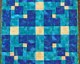 May include: A quilt with a geometric pattern of blue and teal squares with a yellow center square. The quilt is made of fabric with a swirl pattern.