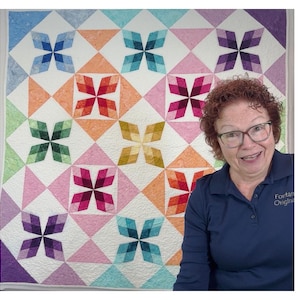 May include: A colorful handmade quilt with a geometric pattern. The quilt features a repeating design of diamond shapes and stylized flower-like motifs in shades of blue, green, orange, pink, and purple. The background is white.