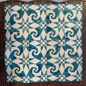 Puede incluir: Una colcha azul y blanca con un patr&oacute;n geom&eacute;trico de formas en espiral. La colcha est&aacute; hecha con una variedad de telas y est&aacute; acolchada con hilo blanco.