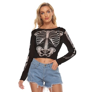 Puede incluir: Top corto negro de manga larga con un estampado de esqueleto blanco detallado en la parte delantera y en los brazos. El top tiene un cuello redondo y un dobladillo corto. La modelo lleva shorts vaqueros azules.