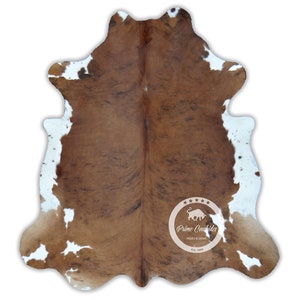 以下が含まれることがあります： 茶色と白の模様が自然なカウハイドラグ。ラグは不規則な形で、明るい色の縁があります。ハイドはPrime Cowhides、Est. 1989からです。