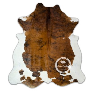 Pode incluir: Tapete de pele de vaca marrom e branco com marcas pretas. O tapete tem um visual natural e rústico e é perfeito para adicionar um toque de estilo western a qualquer cômodo.