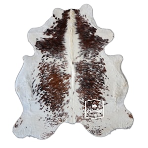 以下が含まれることがあります： 白地を背景に、茶色の斑点とパッチの自然な模様が特徴の牛革ラグ。ラグは不規則な形状で、柔らかく質感のある外観です。インテリアデコレーションに適しています。