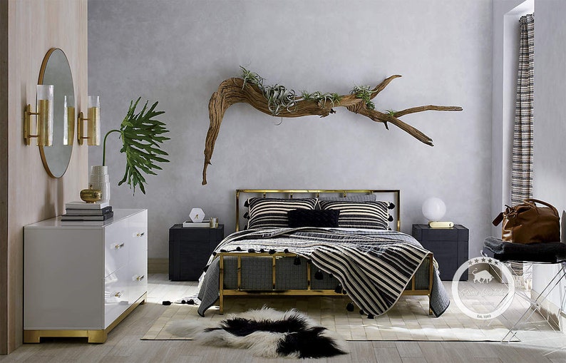 K&ouml;nnte beinhalten: Ein Bettgestell aus goldenem Metall mit einer schwarz-wei&szlig;en gestreiften Bettdecke und einer &Uuml;berwurfdecke. Das Bett steht in einem Schlafzimmer mit einer wei&szlig;en Kommode, einem Treibholzast mit Pflanzen und einem runden Spiegel.