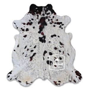 以下が含まれることがあります： ユニークな斑点模様の牛革ラグ。ラグは、不規則な黒と茶色の斑点のある白いベースが特徴です。革は不規則な形状で、自然なエッジがあります。Primeland Cowhidesのロゴが見えます。