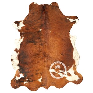 以下が含まれることがあります： 茶色と白の牛革の敷物で、自然な斑点模様があります。敷物は約1.5メートル×2.1メートルです。