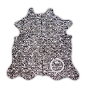以下が含まれることがあります： 白と黒のゼブラ柄のカウハイドラグ。ラグは、丸みを帯びたエッジと自然な革の外観を持つ不規則な形状をしています。円形のロゴが右下隅に表示されています。