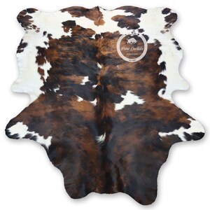 May include: Brown, black, and white cowhide rug with a natural, spotted pattern. The rug is made from a real cowhide and has a rustic, western feel.