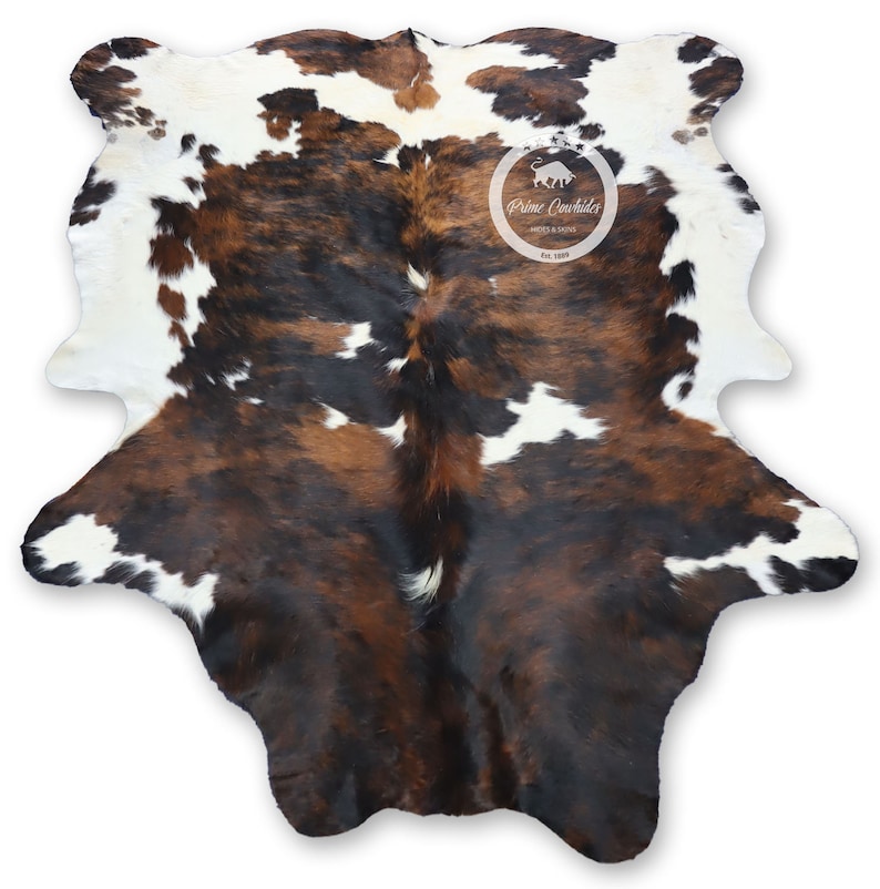 May include: Brown, black, and white cowhide rug with a natural, spotted pattern. The rug is made from a real cowhide and has a rustic, western feel.