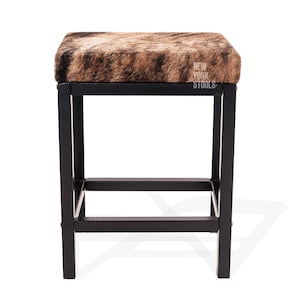 Puede incluir: Un taburete cuadrado con asiento de piel con estampado animal marr&oacute;n y negro y estructura de metal negro. El asiento tiene el texto blanco NEW YORK STOOLS impreso en el lado derecho. La base incluye cuatro patas rectas unidas por barras.