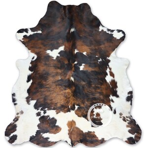 May include: A brown, black, and white cowhide rug with a natural, spotted pattern. The rug is made of real cowhide and has a soft, luxurious feel.