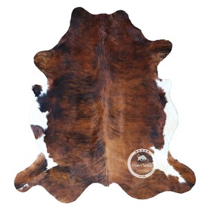 以下が含まれることがあります： 茶色と白の牛革の敷物で、自然な斑点模様があります。敷物は約1.5メートル×2.1メートルです。