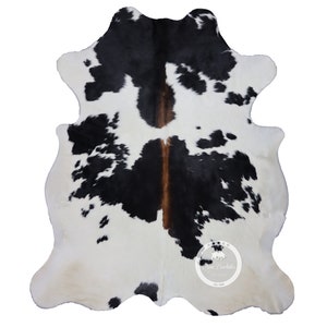 以下が含まれることがあります： 黒と白の牛革の敷物で、茶色のアクセントが付けられています。敷物は自然で不規則な形をしており、柔らかくふわふわとした質感です。