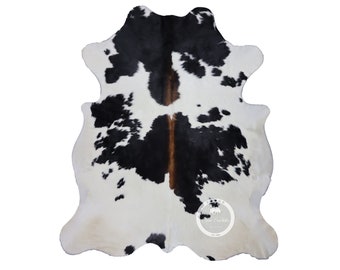 May include: Black and white cowhide rug with brown accents. The rug has a natural, irregular shape and a soft, plush texture.