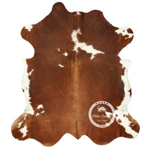 以下が含まれることがあります： 茶色と白の牛革の敷物で、自然な不規則な形をしています。敷物は茶色の背景に白い斑点があります。