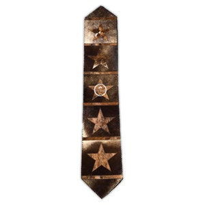 Puede incluir: Una corbata marrón y dorada con un patrón de estrellas. Las estrellas están hechas de un material diferente al resto de la corbata y tienen una textura ligeramente en relieve.
