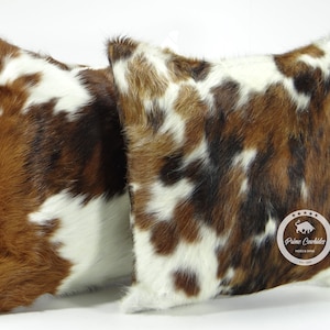 Puede incluir: Dos cojines de tiro de piel de vaca marrón, blanco y negro con una etiqueta de cuero marrón que dice "Prime Cowhides Hides & Skins" en el cojín de la derecha.