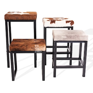 Puede incluir: Cuatro taburetes cuadrados con marcos de metal negro y asientos de piel de vaca en varios tonos de marr&oacute;n, blanco y gris. Un asiento presenta el texto NEW YORK STOOLS. Los taburetes est&aacute;n dispuestos a diferentes alturas con patrones.