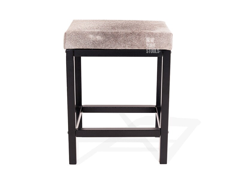Puede incluir: Un taburete cuadrado con un asiento de piel animal texturizada en gris claro y blanco y una estructura de metal negro. El asiento presenta el texto blanco NEW YORK STOOLS impreso en el lado derecho. La base consta de cuatro patas rectas.